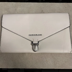 Vit väska  - Vit kuvertväska från Calvin Klein Jeans!  - Brun inuti - ca 28 cm bred  - ca 17 cm hög    Använd endast 1 gång, väldigt gott skick. 