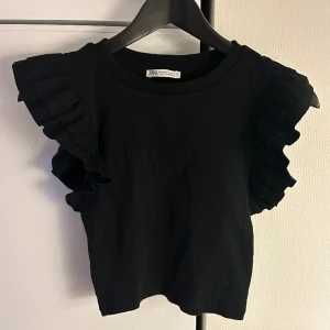 Topp - Super fin svart topp med volanger på axlarna. Är köpt ifrån zara 
