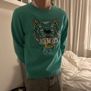 Kenzo Paris tröja - Denna tröja från märket Kenzo Paris i en snygg grön färg. Plagget har använts sparsamt men säljs då jag inte längre använder det. Tröjan är från Kenzos barnkollektion i storlek L men passar personer som bär S/M.