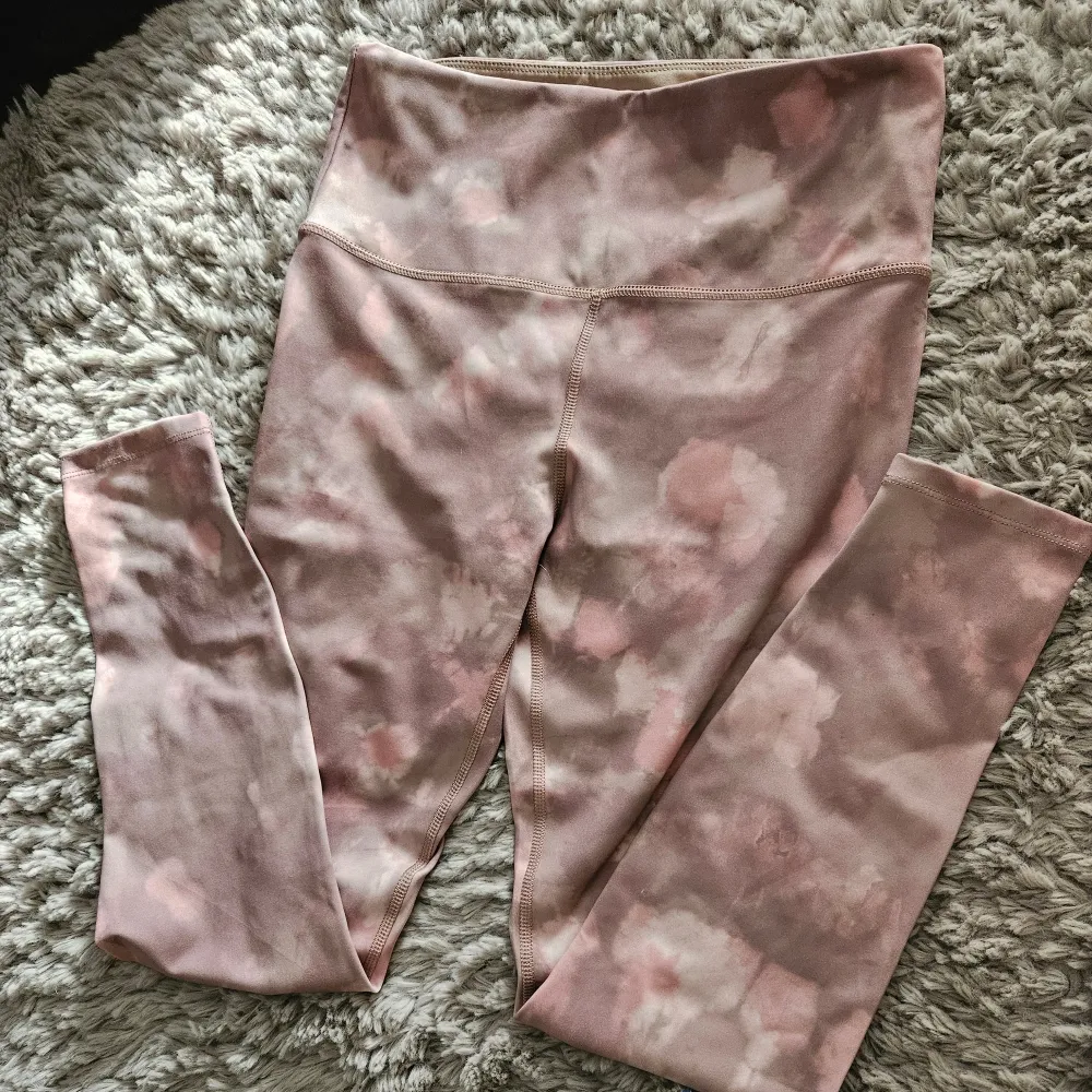 Ett par rosa leggings med ett subtilt mönster i olika nyanser av rosa och beige. Leggingsen har hög midja och är tillverkade i ett stretchigt material som ger en bekväm passform.mobilficka på insidan. Sportswear.