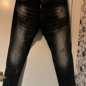 Svarta jeans från Dsquared2 - Ett par svarta jeans från Dsquared2 med slitna detaljer och vita färgstänk. Jeansen har en smal passform och är tillverkade i Italien.