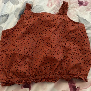 Rostfärgad prickig topp från H&M - En rostfärgad topp från H&M med svarta prickar. Toppen har breda axelband och en elastisk nederkant.