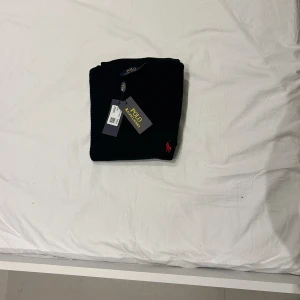 Svart stickad tröja från polo Ralph lauren - En svart tröja från Polo Ralph Lauren med en röd broderad logotyp på bröstet. Tröjan är ny med etikett.