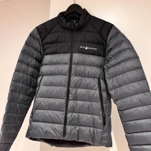 Dunjacka - Jackan är i storlek M och i nyskick. Den är tillverkad av högkvalitativt material och har en bekväm passform.   Den är perfekt för att hålla dig varm och stilfull under kyliga dagar. Passa på att lägga vantarna på denna snygga jacka till ett bra pris