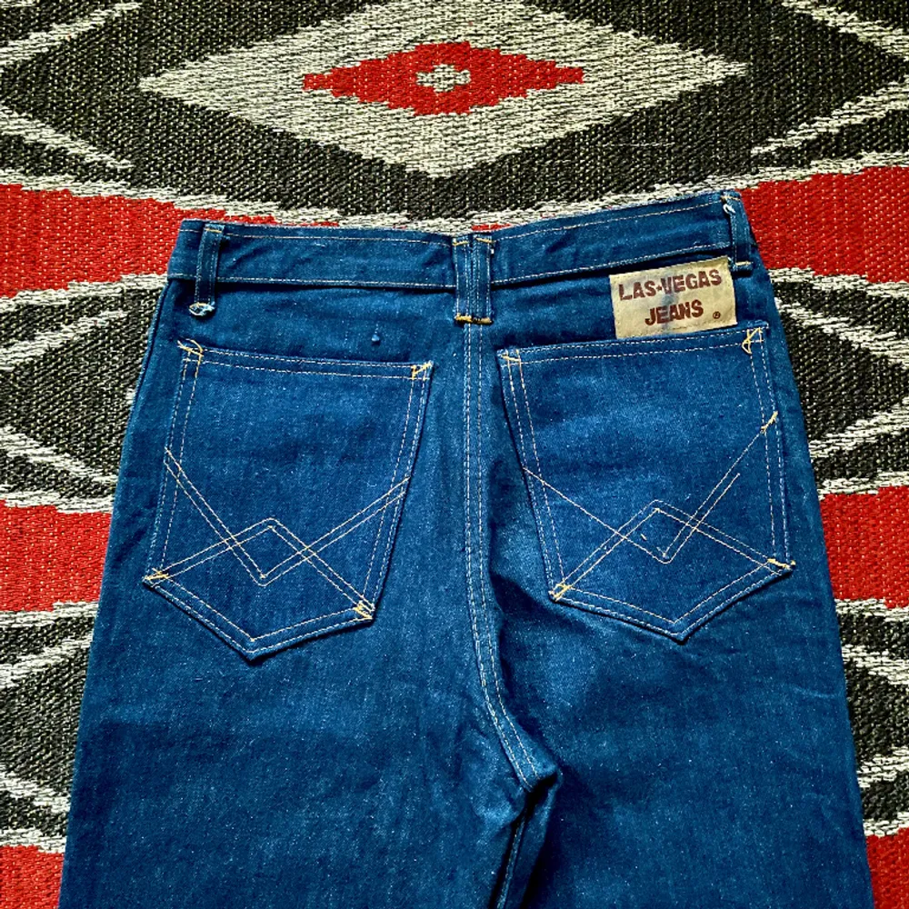 Asballa jeans med läderdetaljer av Las Vegas på 70-talet. Bra skick, några stygn saknas på höger bakficka och färgen har blött in på mocka-lappen i bak.  Midja 34cm Höfter 43cm Gren 28cm Längd 120cm Innersöm 92cm Ofållade byxben  100% bomull. Jeans & Byxor.