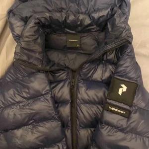 Blå Peakperformance jacka - Blå glansig färg och kan användas höst, vinter och vår, storlek xs så det funkar på dem som är runt 160-165 cm.