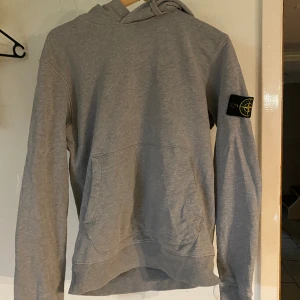 Grå Stone island hoodie - Storlek M Skick 9/10 bara ett litet hål på armen (Du får se den när du ska köpa). Köpt på NK för 2900kr