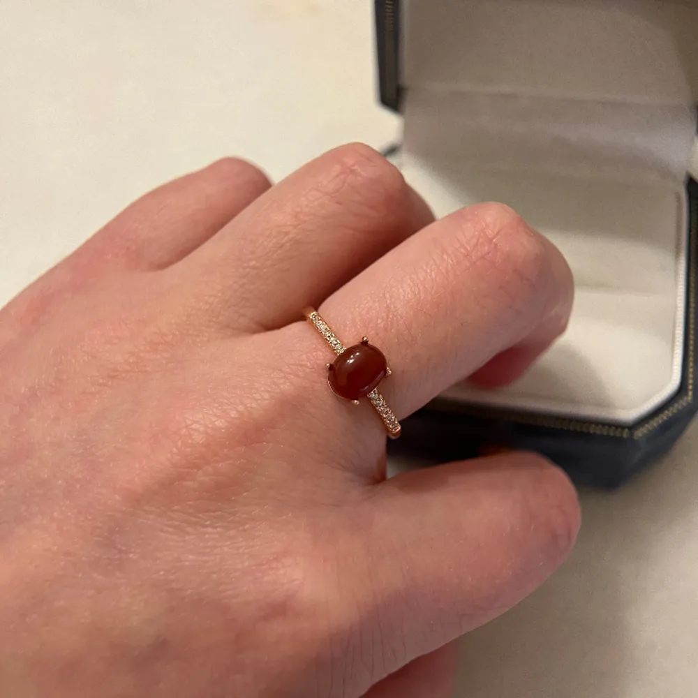 The ring is made of S925 silver with tag on it. Rose gold plated, genuine red jade, besides it are zircons. The Ring is adjustable size. Brand new, with jewellery bag provided . Accessoarer.