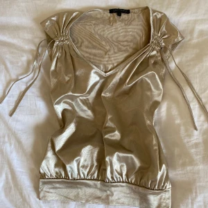 Guldig festtopp - Guldig festtopp i storlek S från Saint Tropez💛 Plagget har ett pyttelitet hål på baksidan vid lappen (syns på bild 3), men det märks inte alls när man har på sig den😊  OBS: Plick ger toppen en konstig textur på bilderna, men den ser inte ut så irl!!