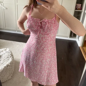 Rosa sommarklänning - Köpt från bershka för ca 3 år sen men har bara använt den 1-2 gånger. Jag säljer den för den tyvärr är lite för liten för mig (kan inte dra upp dragkedjan i sidan riktigt) Man kan justera längden på banden vid axlarna och bysten genom att knyta!