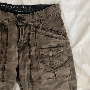 Lågmidjade jeanse  - Lågmidjade camouflage byxor. Utsvängda ben. Knappt använda. Köparen står för frakt.