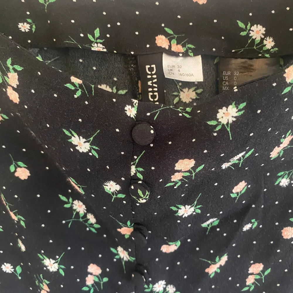 Svart midikjol med blommigt mönster från H&M i storlek 32. Den har fina knappar där fram som detaljer och har även en slits. Den är använd men i fint skick. Kjolar.