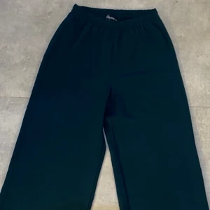 Tygbyxor- mörkgröna  - Mörkgröna tygbyxor med vida ben i tunt och slätt material samt resår runt midjan. Använd endast ett par gånger och har helt nytt skick.