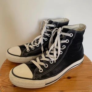 Svarta High-Top Converse - Svarta high-top converse. Storlek 39.5. Använt skick. Fläckar på skosnörena, gummisömmen på insidan av skorna börjar gå upp, loggan baktill börjar försvinna.