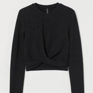 Glittery top (oanvänt)  - Kort svart topp i mjuk jersey med glitter. Rund halsringning , långa ärmar och omlott drapering i fållen. Tröjan är som en magtröja o slutar vid midjan/under bröstet. Helt oanvänt med prislapp på. 