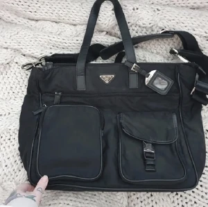 Prada bag väska axelremväska - Från butik! Felfritt skick, ärvd så finns inget kvitto men väskan är äkta. Lite mer än 40 cm bred och lite under 15cm djup. Massor med fickor och förvaring. Perfekt för skola, resor, jobb! Kom med bud <3 glöm inte att kolla övriga annonser för fynd