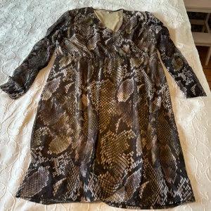 Figur smickrande klänning  - Ormskinnsmönstrad klänning i strl XL. Fodrad. Lätt gemenskinlig på ärmar. I mycket gott skick. Stretchig. 