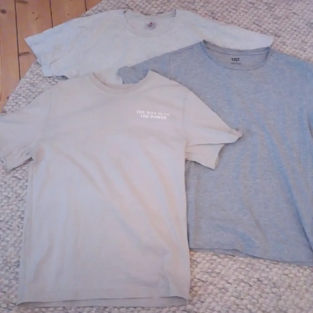 Ett paket med tre T-shirts. I gott använt skick. Färgenrna är grå, ljusgrå och en beige t-shirt med tryck på både fram och baksida.. T-shirts.