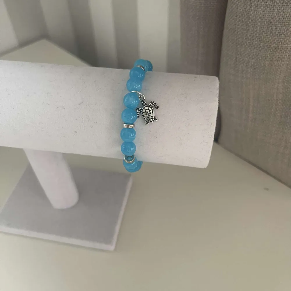 Egengjort pärlarmband med blåa och silvriga pärlor. Armbandet har en berlock som avbildar en sköldpadda. . Accessoarer.