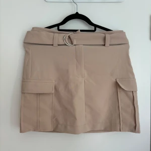 Kjol - Säljer denna beiga kort kjol med skärp då den inte kommit till användning senaste tiden. Super snygg och lätt att styla