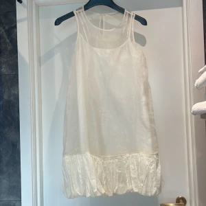 Vit ärmlös klänning med volangdetalj - En vit ärmlös klänning med volangdetalj vid nederkanten. Klänningen har en lös passform och är tillverkad i ett lätt och luftigt material, vilket gör den perfekt för varmare väder.underklänning då klänningen är transparent. inte kritvit. 