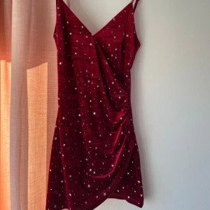 Rödklänning - Jättesöt rödklänning med silvriga stjärnor, passar perfekt till t.ex. julfester. Använd en gång, den är en aning kort för mig som är 177cm så rekommenderas till någon som är lite kortare. Väldigt skön på och stängs i ryggen med dragkedja. 