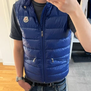 Moncler väst  - Svin fett blå moncler väst denna är blå ser lilla ut på bild. Super fräsch inga märken eller sånt. Säljer då den har blivit för liten:( och såklart är den äkta, kommer med en påse som man kan lägga den i och ett brev från moncler