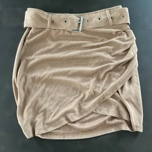 Kjol NAKD - Kjol från Linn Ahlborgs kollektion för NAKD. Mockaimitation med bälte. Strl 34. Snygg ihop med ett par boots!