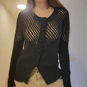 Y2K svart stickad tröja med knappar - Inköpt mellan år 2000-2010. Svart stickad y2k tröja med öppningar längs axlarna samt knappar framtill. Väldigt häftig både till jeans och kjol. Superskick! Passar S och XS. Svarar på alla frågor.