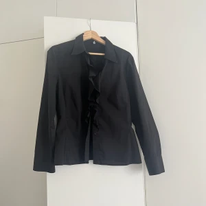 Skjorta med volanger - Svart skjorta/blus med volanger köpt på en secondhandmarknad i Italien, därav vet jag inte märket. Figursydd. Jättebra skick