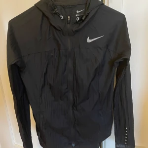 Vindjacka nike - Svart praktisk och snygg vindjacka från nike i storlek xs. Har ett litet märke på nacken men det syns inte när man har på sig jackan då det är under luvan💓