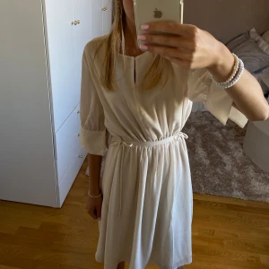 Beige klänning från H&M - Säljer en superfin beige klänning från H&M i storlek XS. Klänningen har trekvartsärmar och ett knytband i midjan som ger en snygg passform. Perfekt för både vardag och fest! 💖