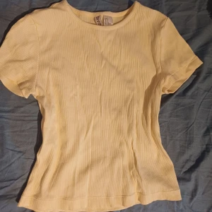 Gul ribbad t-shirt från Divided - Säljer en superfin gul t-shirt från Divided. Den är ribbad och har en normal passform. Perfekt för sommaren eller våren! T-shirten är i nyskick och är gjord av bomull, vilket gör den väldigt bekväm att ha på sig. Passar perfekt till både jeans och kjol. 🌼