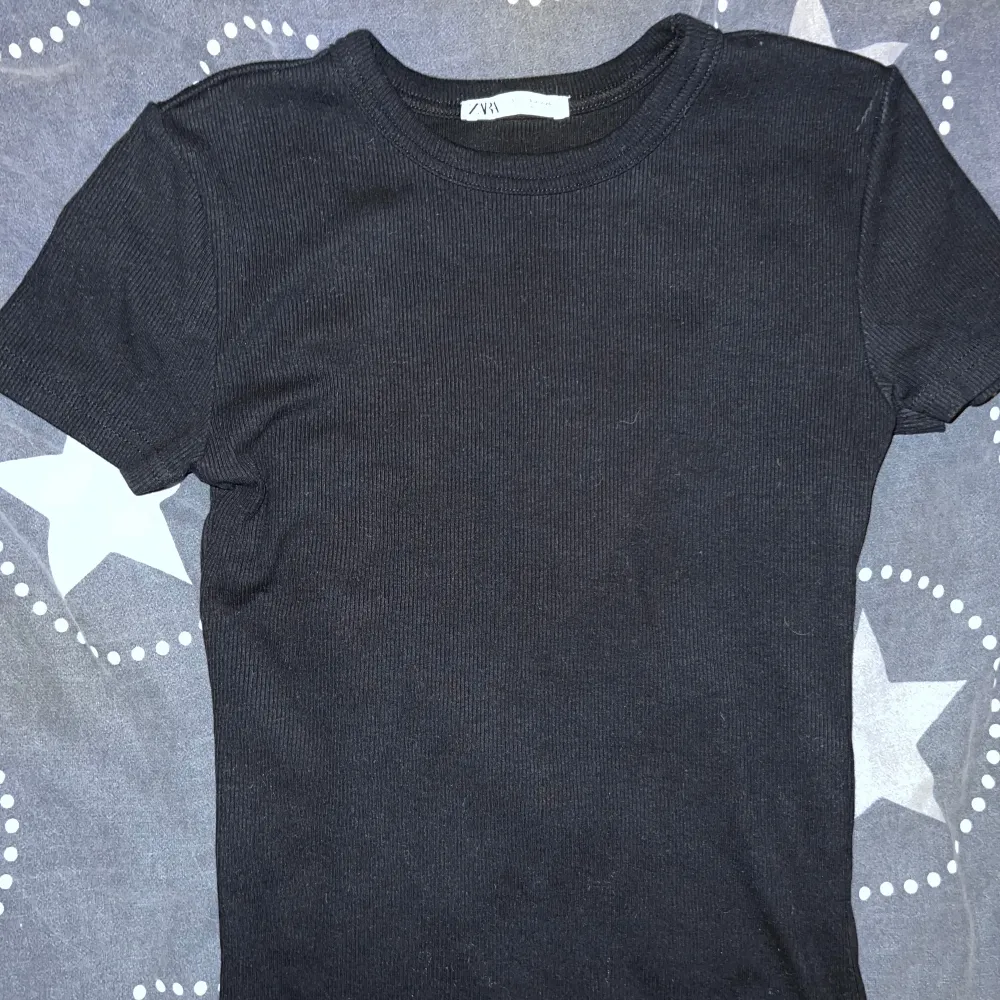 Säljer en svart ribbad t-shirt från Zara i storlek S. Den är kortärmad och har en tight passform som framhäver figuren. Perfekt för både vardag och fest! 🖤. Toppar.