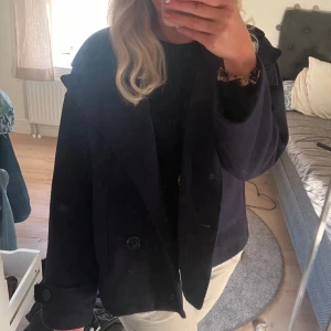 Svart kappa med knappar - Säljer en snygg mörblå kappa med knappar från Design By Si. Den är perfekt för höst och vår, och har en klassisk stil som passar till det mesta. Jackan är långärmad och har en normal passform. Den är i mycket bra skick och redo för en ny ägare! Nypris 849kr!