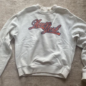 Vit sweatshirt från H&M med New York-tryck - Säljer en vit sweatshirt från H&M i storlek XS. Tröjan har ett coolt New York-tryck i rött och blått på framsidan. Den är supermjuk och perfekt för höst och vinter. Passar både till vardags och chillkvällar. Skicka ett meddelande om du är intresserad!