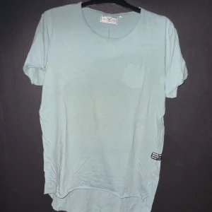 Ljusgrön t-shirt från Denim Day - Säljer en ljusblå t-shirt från Denim Day. Den har en bröstficka och en liten etikett på sidan. T-shirten är i bomull och har en normal passform. Perfekt för sommaren!