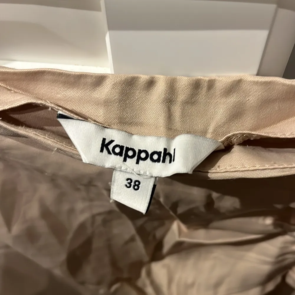 En beige kjol från Kappahl med rynkade detaljer på framsidan. Kjolen har en slits på sidan och är tillverkad i ett glansigt material.. Kjolar.