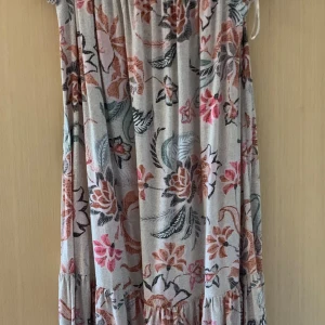 Blommig klänning från Lindex - Säljer en superfin blommig klänning från Lindex. Den är i storlek M och har ett härligt mönster med blommor i rosa, rött och grönt på en beige bakgrund. Klänningen är ärmlös och har en lös passform med volangdetaljer längst ner. Perfekt för sommarens alla fester eller en skön dag på stan!