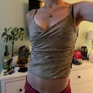 Leopardmönstrad linnetopp - Säljer en snygg leopardmönstrad linnetopp i beige och bruna nyanser. Toppen har smala axelband och en omlott-design framtill som ger en smickrande passform. Perfekt för en utekväll eller fest! 🐆✨