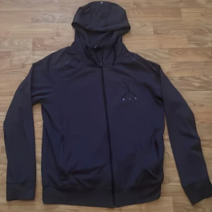 Svart träningsset från Jordan - Säljer ett blå träningsset från Jordan. Setet består av en hoodie med dragkedja och matchande byxor. Perfekt för träning eller en avslappnad dag. Hoodien har en snygg logga på bröstet och byxorna har en bekväm passform.