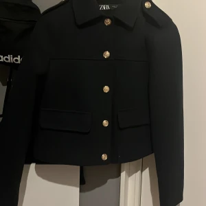 Mörkblå kappa frpn zara  - Säljer en snygg mörkblå kavaj från Zara.kag köpte den för 600kr och har använt den 2-3 gånger. säljer den för vill köpa en ny!Den har guldknappar fram och på axlarna. Kavajen är croppad och har en normal passform. Perfekt för både