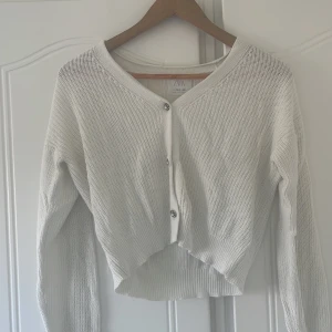 Vit cardigan - En vit kofta med silverknappar. Koftan är luftig och stickad.