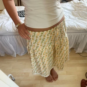 blommig mönstrad midikjol - gul och grön blommig midikjol med vit spets längst ner. bra skick!! står storlek S men skulle säga att den passar XS-L eftersom resåren i midjan är stretchig. längd: 57 cm 