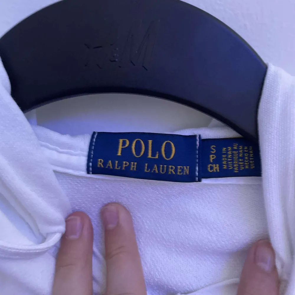 En vit huvjacka från Polo Ralph Lauren med dragkedja framtill och två fickor. Jackan har en broderad logotyp på bröstet och en huva med dragsko.. Jackor.