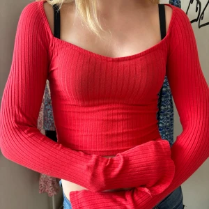 Röd ribbad topp - En röd ribbad topp med långa ärmar och en tight passform. Toppen har en fyrkantig halsringning och är croppad i modellen. Den har även slit längst ner i ärmarna. Använd ett fåtal gånger.