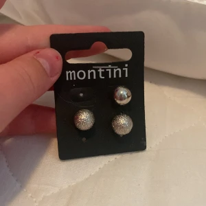 Örhängen från Montini - Ett par örhängen från Montini. Ett par är silverfärgade med en slät yta och det andra paret är silverfärgade med en glittrig yta.