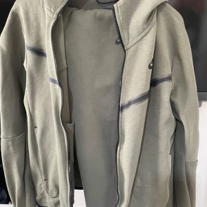 Grönt Techfleece Set från Nike - En grön tech fleece från Nike med dragkedja och huva. Byxor i samma färg men storlek L med öppen mudd