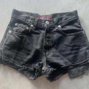 Svarta jeansshorts från Levi's - Ett par svarta jeansshorts från Levi's med råa kanter och fyra fickor. Shortsen har en knapp och dragkedja framtill samt bälteshällor. 