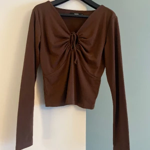 Topp - Brun topp från BikBok, långa ärmar, v-ringning och knytning vid bröstet. Något kortade modell. Storlek M. Använd ca 2-3ggr. 